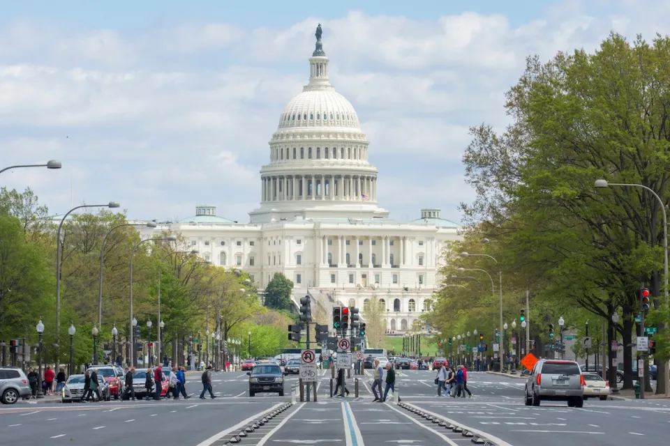 People crossing the street in a crosswalk with U.S. capitol dome visible in background on Pennsylvania Avenue in Washington DC.